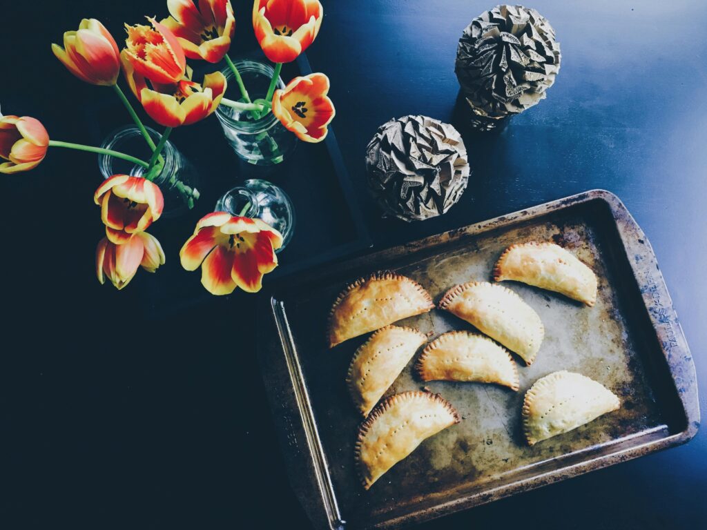 A rustic tray of empanadas alongside vibrant tulip flowers in glass vases.