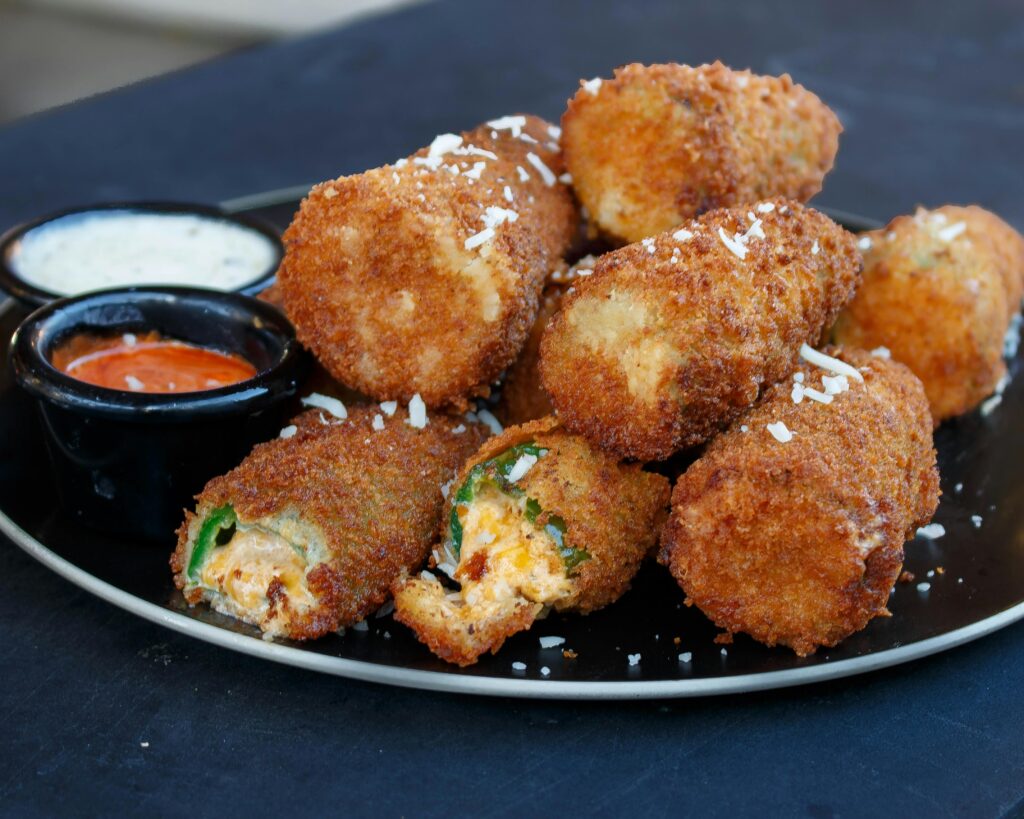 Mouthwatering fried jalapeño poppers on a plate with two delicious dipping sauces.