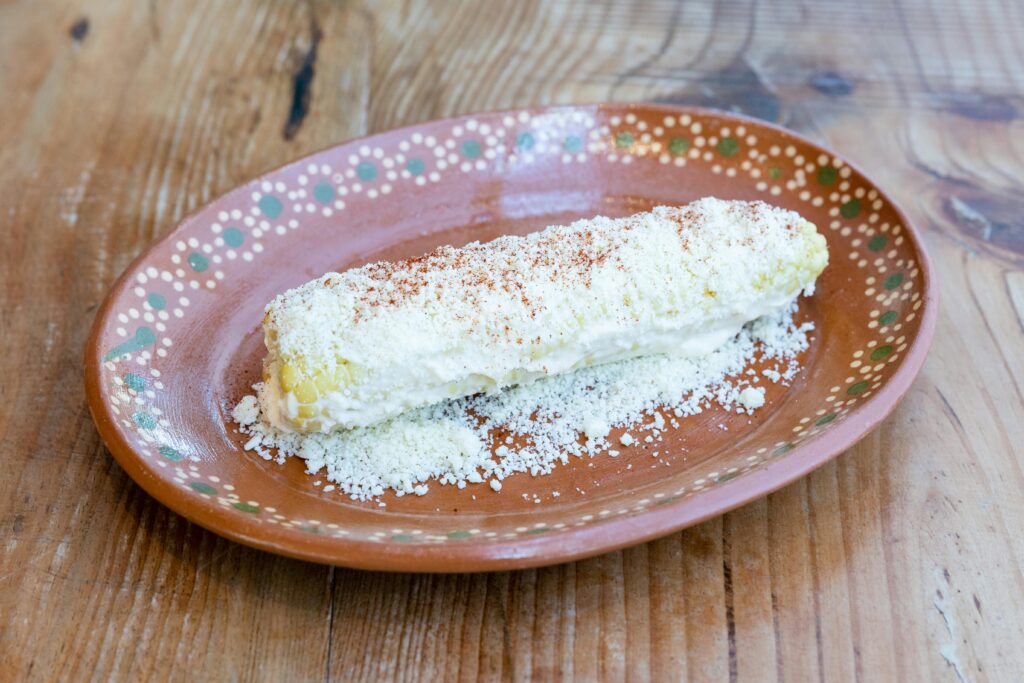 Close-up of traditional Mexican elote garnished with cheese and paprika on a rustic plate.